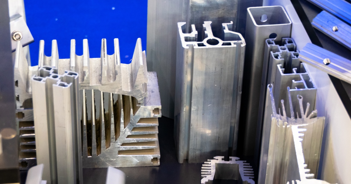 A variety of aluminum profiles with different shapes laid out on a black surface against a blue background.