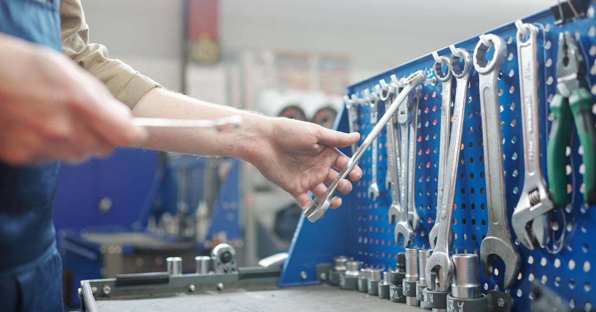 A person picking up a tool from a workbench. All the tools hang neatly on the wall of the workbench.