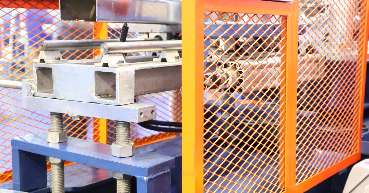 An orange machine safety guard that prevents worker injuries from a cold rolling machine. The machine is in a facility.