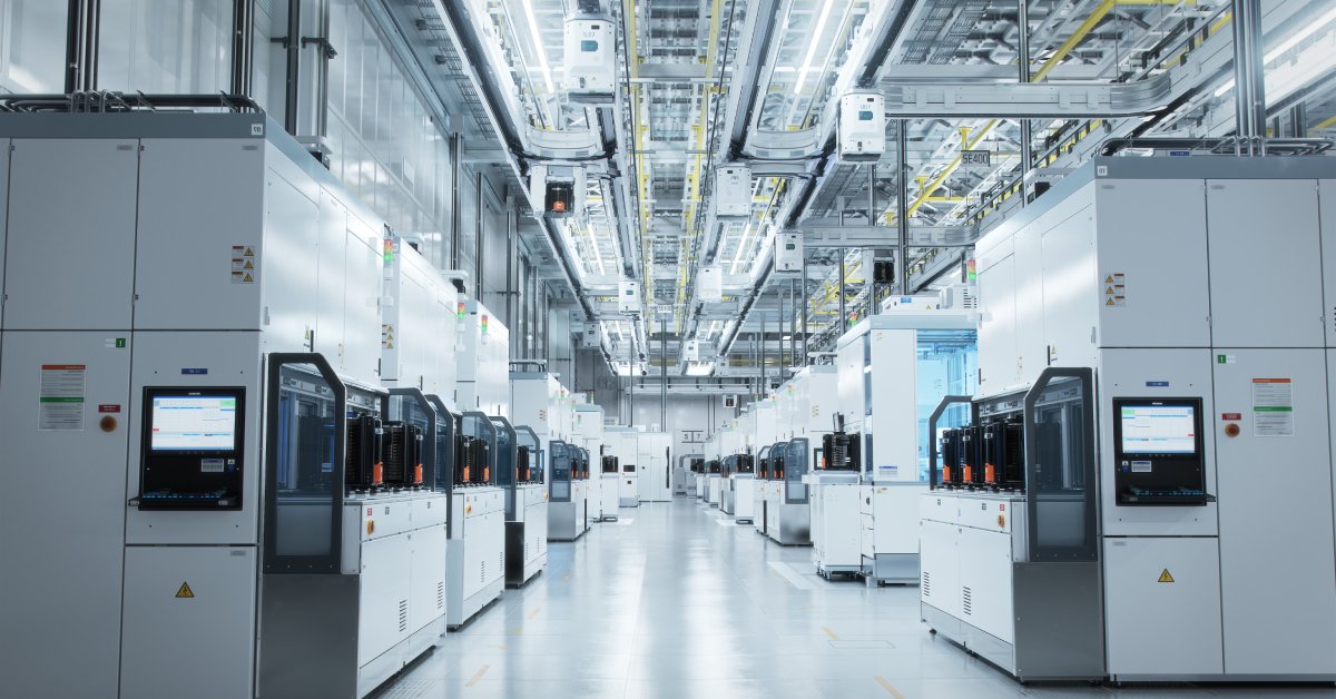 A bright cleanroom in a facility with a row of large machines extending down the room. Overhead is a water transfer system.