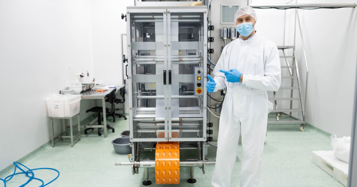 A worker in a cleanroom with a piece of machinery behind him. He is wearing safety gear to keep the space clean.