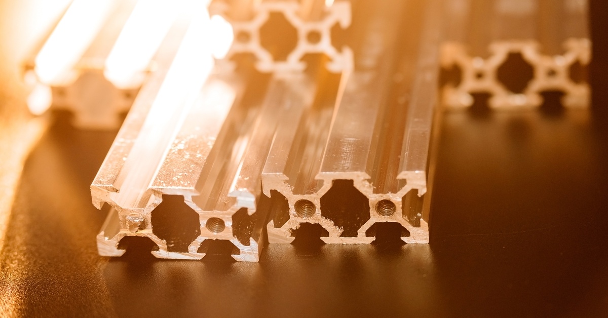 Multiple aluminum profiles of the same design are stacked on each other. A bright light illuminates the stack.